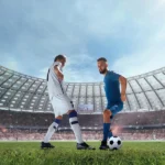 Dos jugadores de fútbol en un estadio, uno vestido de blanco y el otro de azul, se preparan para driblar el balón en un partido emocionante. La multitud en el fondo crea un ambiente vibrante y competitivo.
