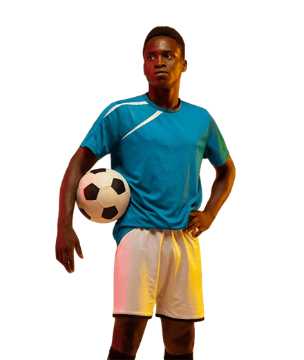 Joven futbolista de pie con una pelota de fútbol en la mano, vistiendo camiseta azul y pantalones cortos blancos, mostrando confianza y actitud deportiva.