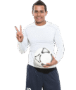 Jugador de fútbol sonriente con balón, vestido con camiseta de manga larga blanca y pantalones cortos oscuros, haciendo un gesto de paz.