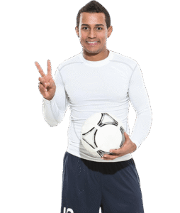 Jugador de fútbol sonriente con balón, vestido con camiseta de manga larga blanca y pantalones cortos oscuros, haciendo un gesto de paz.